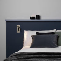 Kleine wandlamp naast het hoofdeinde van een bed met donkerblauwe wand en grijze kussens 30
