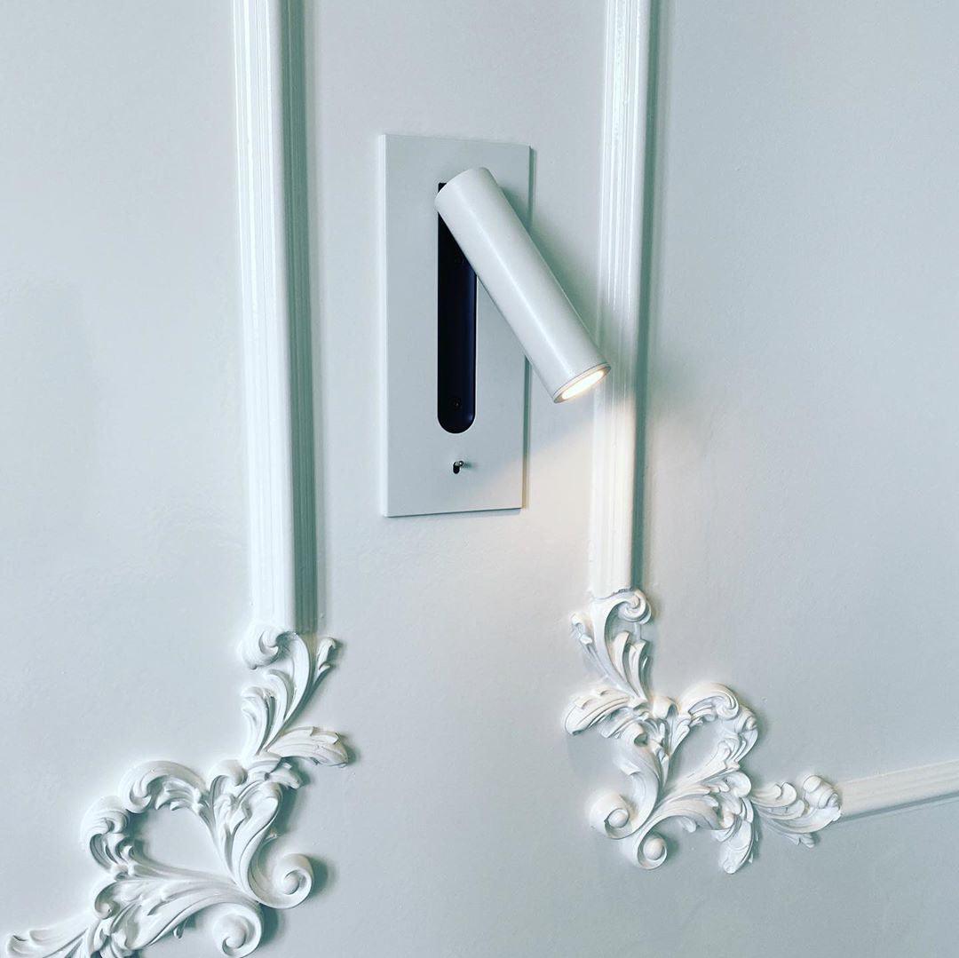 Witte wandlamp ingebouwd in een witte muur met sierlijsten, met brandende, gedraaide spot 27