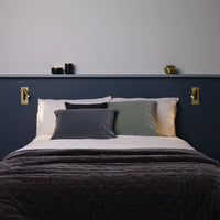 Twee goudkleurige wandlampen aan weerszijden van een bed met donkerblauw hoofdeinde en een plank 35