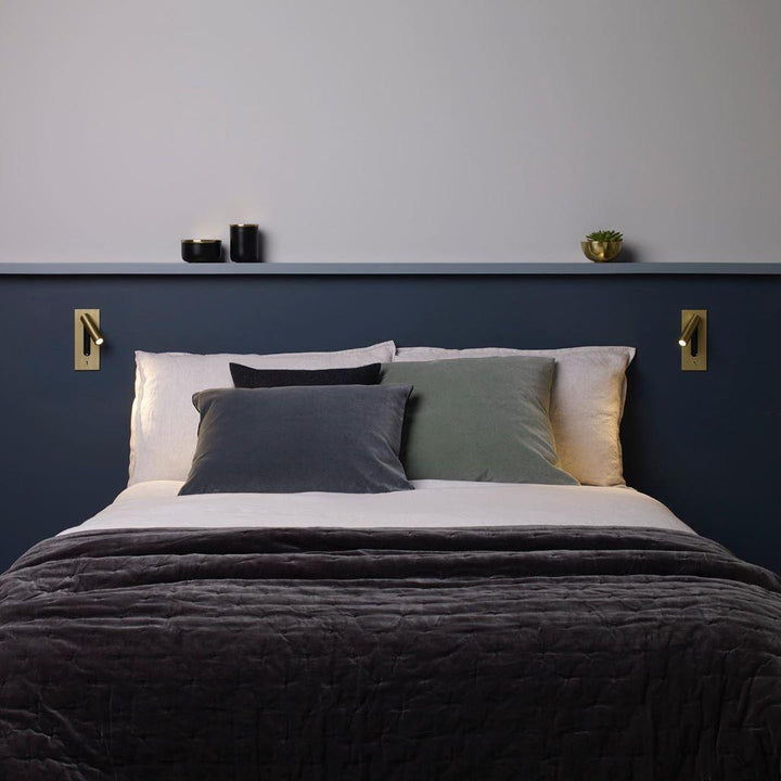 Twee goudkleurige wandlampen aan weerszijden van een bed met donkerblauw hoofdeinde en een plank 35