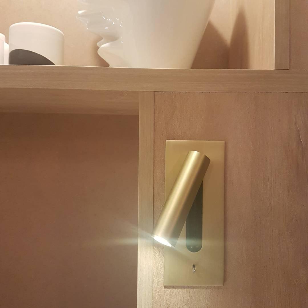 Goudkleurige wandlamp met brandende spot, ingebouwd in een houten kastwand naast een plank 32