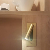 Goudkleurige wandlamp met brandende spot, ingebouwd in een houten kastwand naast een plank 32