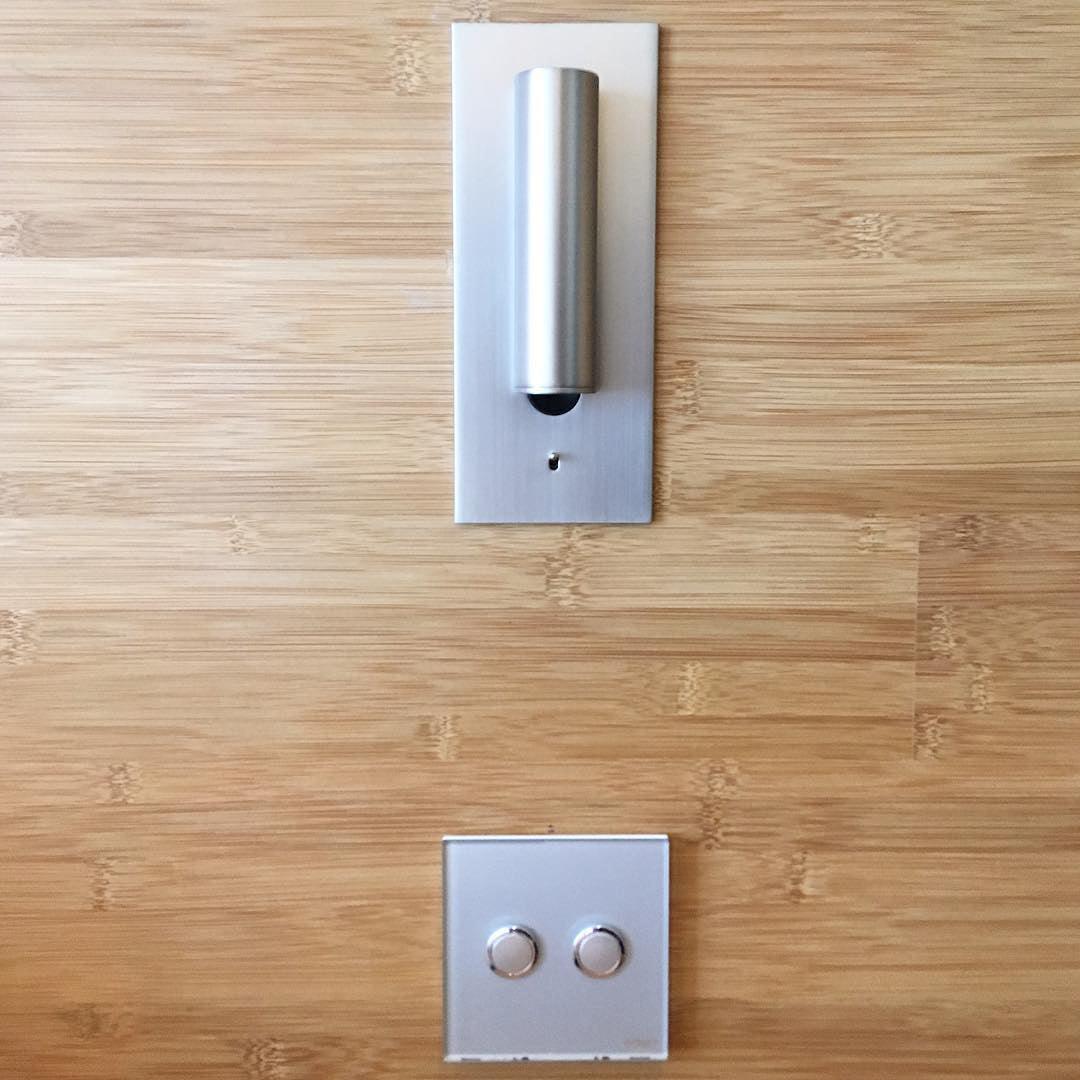 Zilverkleurige wandlamp met rechtopstaande spot in een bamboe wand, met dubbele schakelaar eronder 34