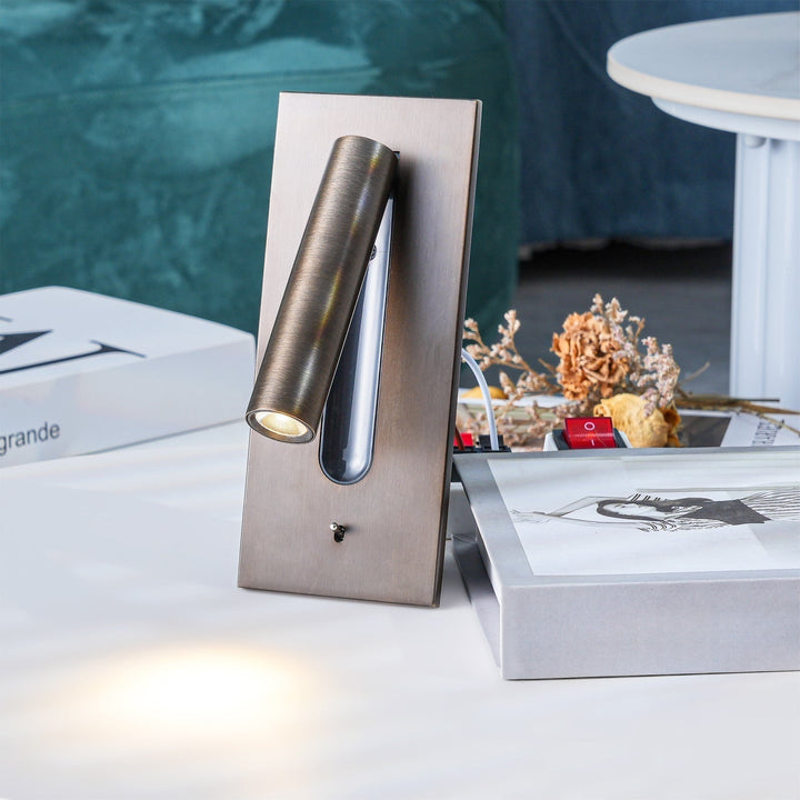 Wandlamp in donker metaal staand op een tafel tussen boeken en droogbloemen, spot brandt 28