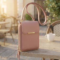 Oudroze uitvoering van de tas op een houten tafel op een zonnig terras, met gouden ritsen, dubbele rits en schouderband. 2