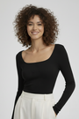 Lachende vrouw met krullend haar draagt de zwarte geribbelde top met lange mouwen, gecombineerd met een witte broek 1