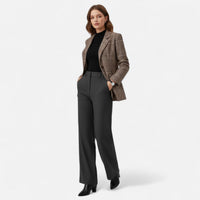 Model in volledige outfit met de blazer over een zwarte top, grijze broek met wijde pijpen en zwarte laarzen, handen in de zakken. 2