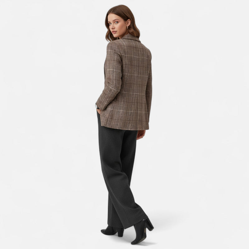 Achterkant van de geruite blazer, gedragen door een model dat over haar schouder kijkt, met grijze broek en zwarte laarsjes. 3