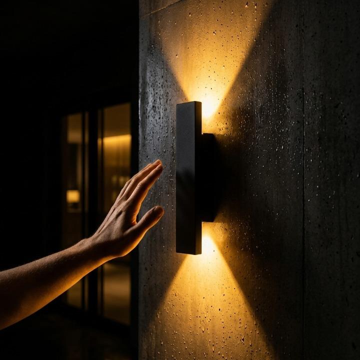Hand strekt zich uit naar een zwarte wandlamp op een betonnen muur met waterdruppels, warm licht omhoog en omlaag 8