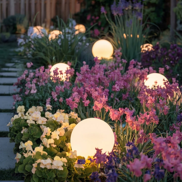Warm gloeiende bollen verspreid tussen roze, paarse en crèmekleurige bloemen langs een tegelpad in de avondschemering. 7
