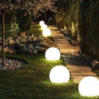 Lichtgevende bollen in verschillende maten langs een tuinpad op het gras, met stenen rand en vijver op de achtergrond. 6