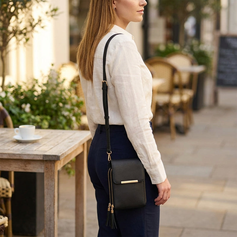 Vrouw in wit linnen overhemd en donkere broek draagt de zwarte tas crossbody, gezien van opzij, met kwastjes aan de ritsen. 7