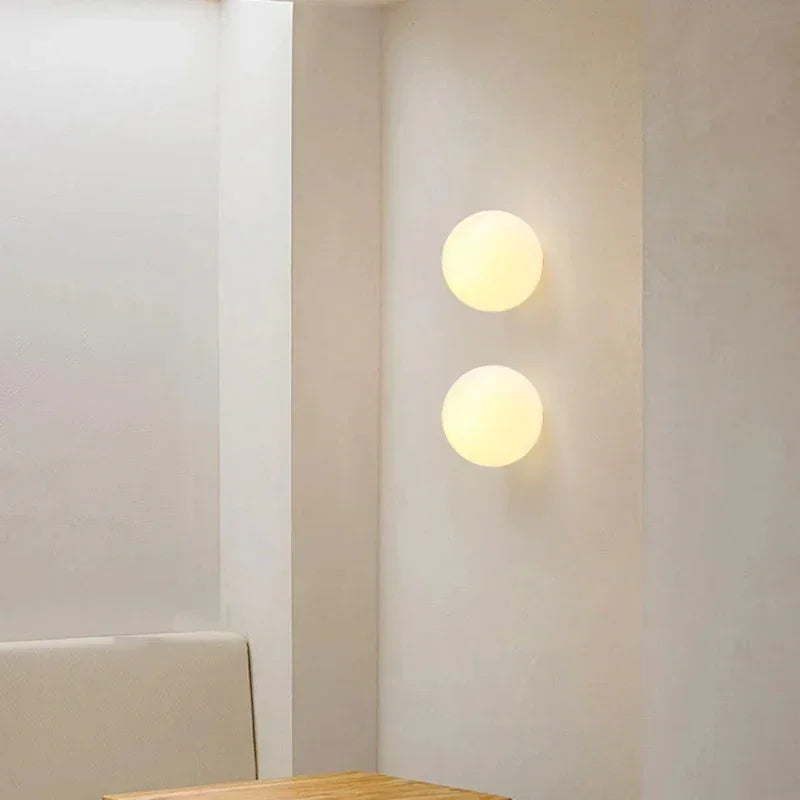 Twee glazen bollampen onder elkaar aan een lichte wand boven een houten tafelblad 15