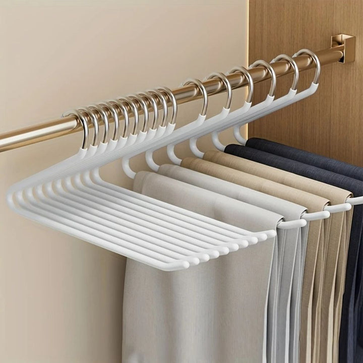 Witte broekhangers aan een kastroede, volgehangen met broeken in beige, grijs en donkerblauw 3