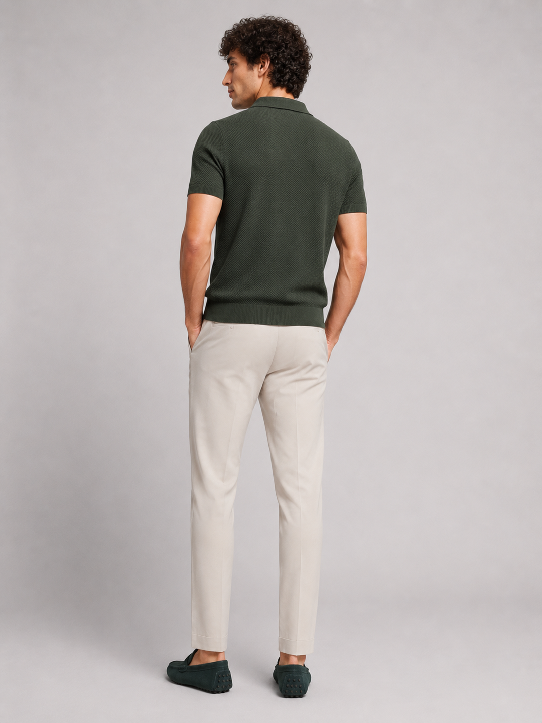Achterkant van het donkergroene poloshirt, model kijkt opzij, met crèmekleurige broek en groene loafers 14