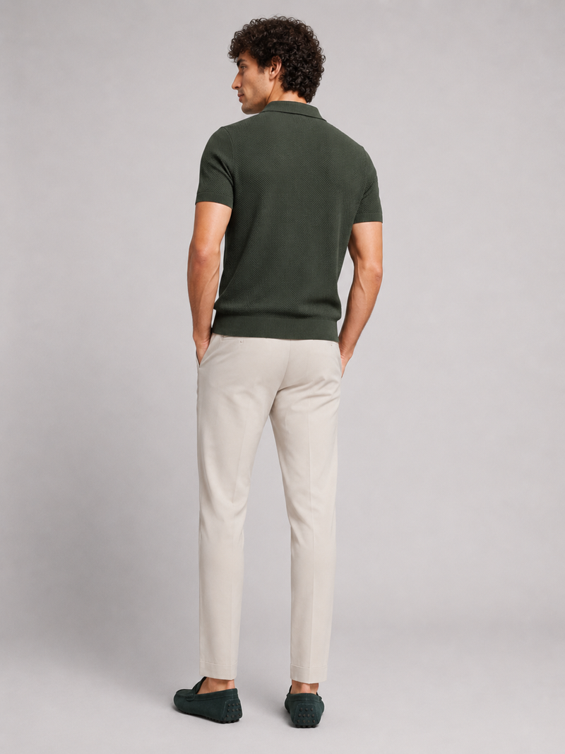 Achterkant van het donkergroene poloshirt, model kijkt opzij, met crèmekleurige broek en groene loafers 14