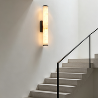 Verticale marmeren wandlamp op een witte trapmuur, naast een trap met zwarte leuning. 7