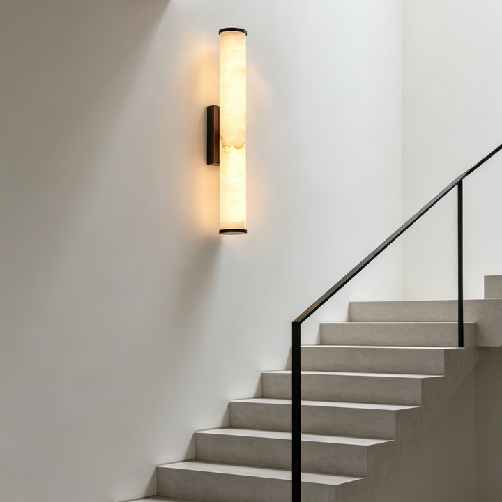 Verticale marmeren wandlamp op een witte trapmuur, naast een trap met zwarte leuning. 7