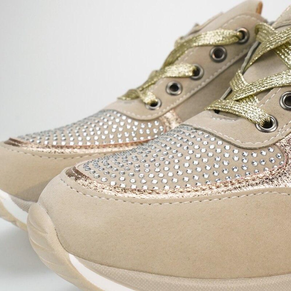 Close-up van de neus van twee beige sneakers met strassteentjes, gouden metallic veters en een witte zool. 10
