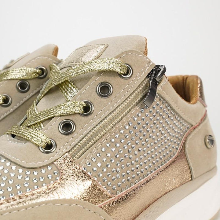 Close-up van beige sneakers met gouden veters, metalen oogjes, zijrits en rijen strassteentjes op de neus. 8