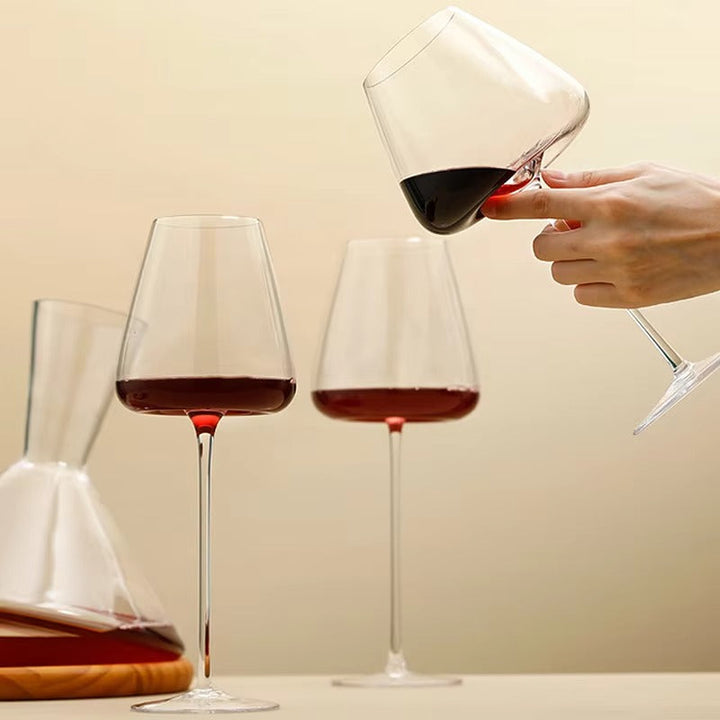 Twee glazen rode wijn op tafel terwijl een hand een derde glas kantelt 9