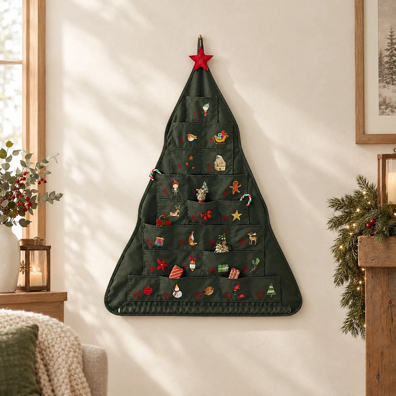 Groene kerstboomvormige adventskalender met 24 vakjes en een rode ster, opgehangen aan een lichte muur in een gezellige woonkamer. 1