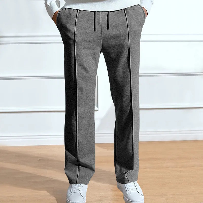 Grijze broek met trekkoord en nette persvouw, op de heupen gedragen met witte sneakers en een witte trui. 2
