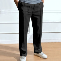 Zwarte broek met trekkoord en persvouw, gedragen door een model met handen in de zakken en witte sneakers. 3