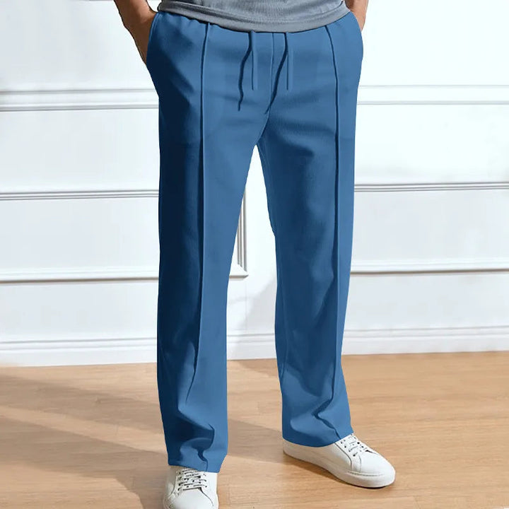 Blauwe broek met trekkoord en persvouw, gedragen door een model met witte sneakers en een grijs shirt. 5