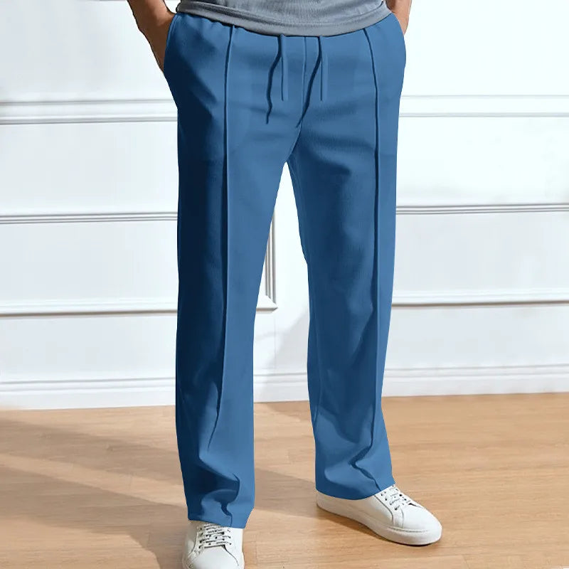 Blauwe broek met trekkoord en persvouw, gedragen door een model met witte sneakers en een grijs shirt. 5