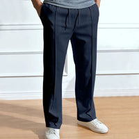 Donkerblauwe broek met trekkoord en persvouw aan de voorkant, gedragen door een model met witte sneakers en grijs shirt. 1