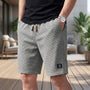 Man draagt een grijze wafelshort met trekkoord en horloge, hand in de zak, op een terras met planten en loungestoel. 6