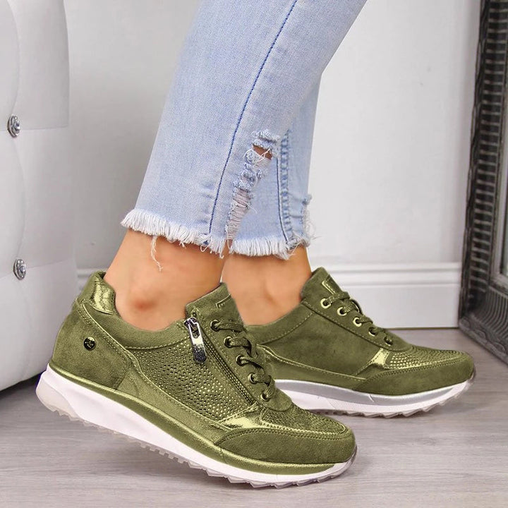 Olijfgroene sneakers met metallic accenten en een rits aan de zijkant, gedragen door een model met gerafelde spijkerbroek. 4