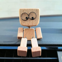 Houten figuurtje met grote ronde ogen zit van voren op de rand van een dashboard, benen over de rand. 4