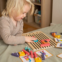 Blond kind speelt aan tafel met het houten puzzelbord, omringd door losse blokken met witte pennetjes en kaarten. 4