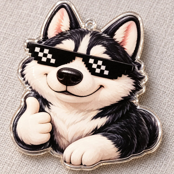 Close-up van een los transparant acryl ornament: een lachende husky met pixelzonnebril en een duim omhoog, op een grijze stoffen ondergrond. 4