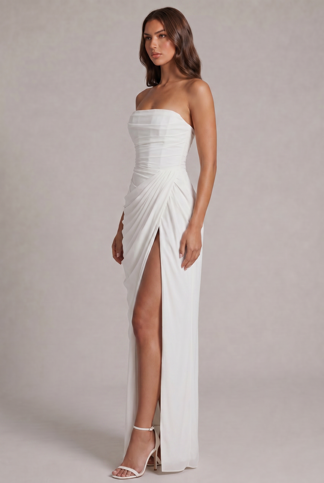 Zijaanzicht van de witte jurk met geplisseerde drapering, hoge split en sandalen met hak 19