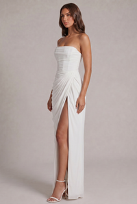 Zijaanzicht van de witte jurk met geplisseerde drapering, hoge split en sandalen met hak 19