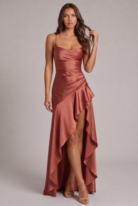 Jurk in terracotta satijn van voren gedshowd, model raakt haar haar aan, met volant en hoge split. 25