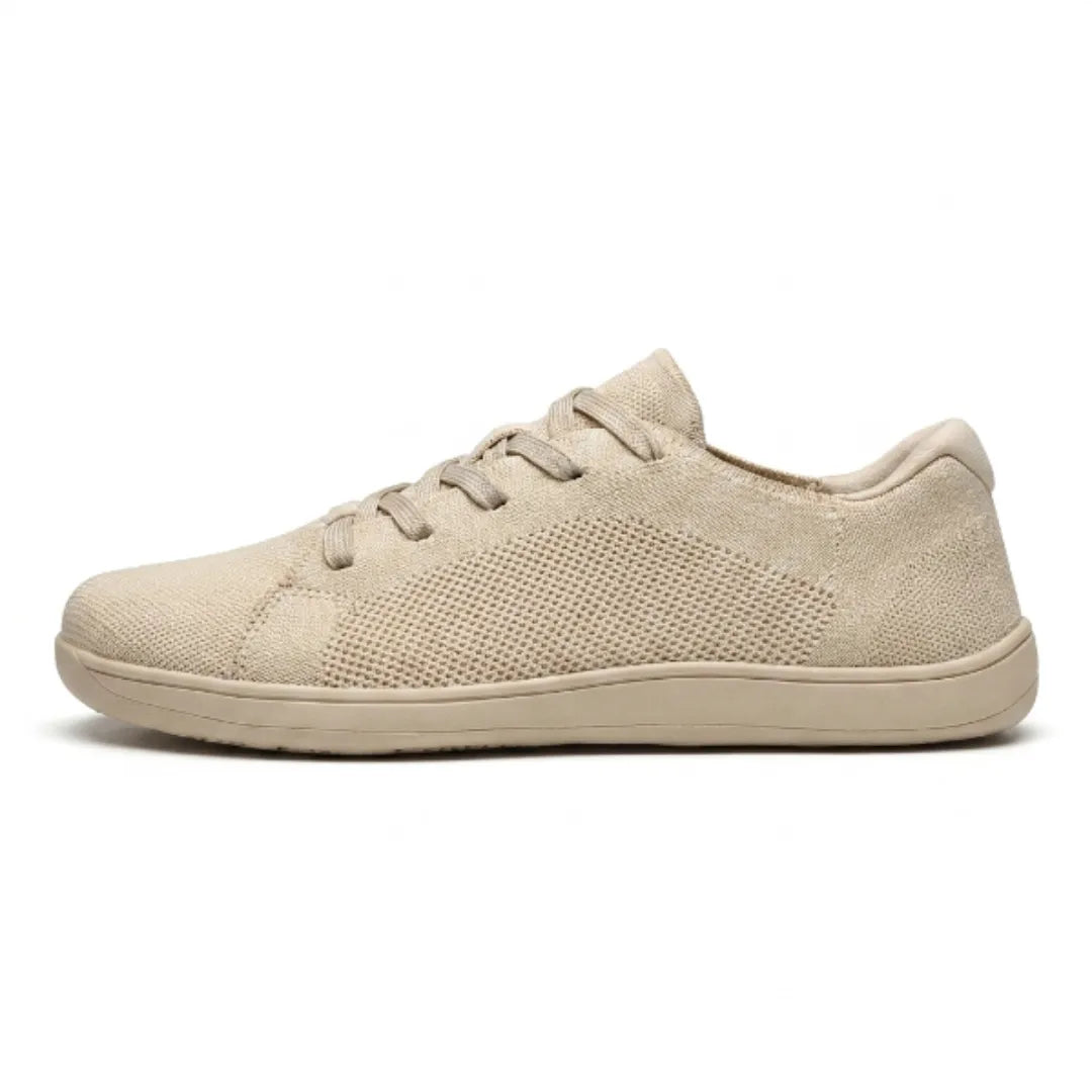 Beige gebreide sneaker van opzij gezien, met veters, ademende gaasvlakken en een effen beige zool op een witte achtergrond. 1