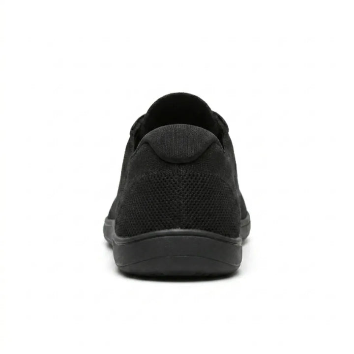 Zwarte gebreide sneaker van achteren, met het gaasdetail op de hiel en de brede, vlakke zool. 18