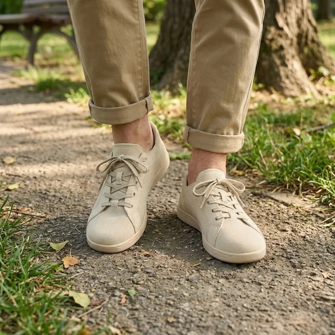 Beige gebreide sneakers gedragen door iemand in een beige broek met opgerolde pijpen, staand op een parkpad met gras. 2