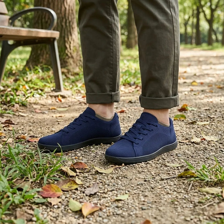 Marineblauwe gebreide sneakers met zwarte zool gedragen met een olijfgroene broek, staand op een parkpad naast een bankje. 20