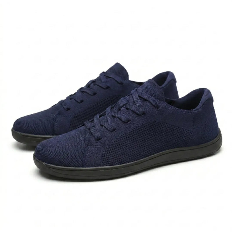 Paar marineblauwe gebreide sneakers met zwarte zool en veters, schuin van voren gezien op een lichte achtergrond. 25