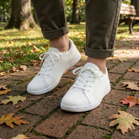 Model draagt de witte gebreide sneakers met witte zool op een bakstenen pad met herfstbladeren, met opgerolde olijfgroene broek. 38