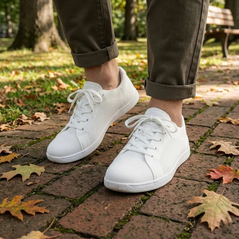 Model draagt de witte gebreide sneakers met witte zool op een bakstenen pad met herfstbladeren, met opgerolde olijfgroene broek. 38