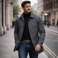 Model in de grijze trenchcoat wandelt door een stadsstraat, jas open gedragen met één hand in de zak. 5