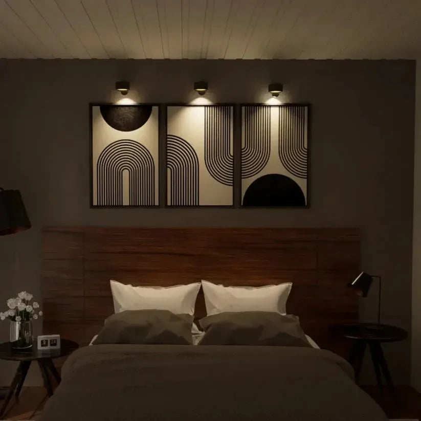Drie zwarte wandlampen verlichten elk een ingelijst schilderij boven een bed in een slaapkamer 10