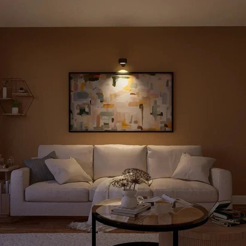 Zwarte wandlamp boven een schilderij belicht het kunstwerk boven een bank in de woonkamer 15