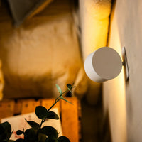 Achterzijde van een witte wandlamp met aanraakknop, gemonteerd op de muur naast een plant 4
